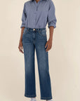 Person wearing a blue button-up shirt and jeans on a beige background