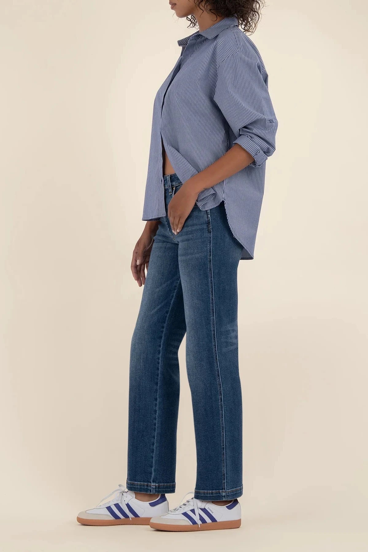 Person wearing a blue shirt and jeans with white sneakers on a beige background