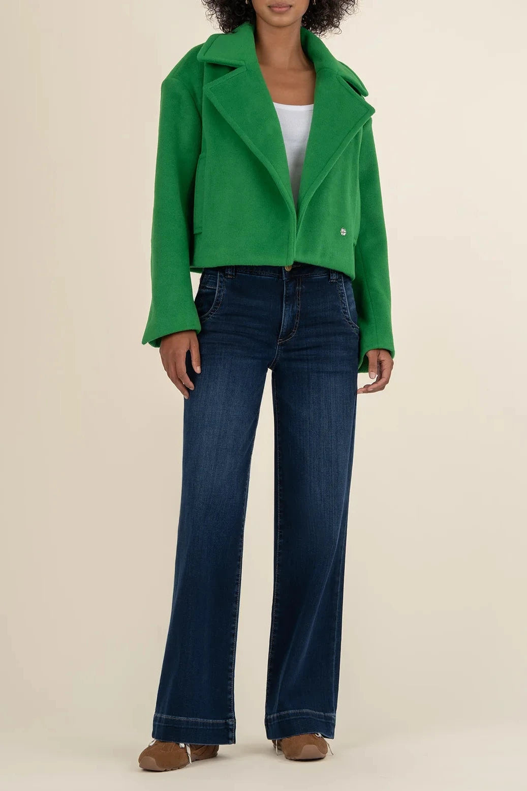 Person wearing a green jacket and blue jeans on a beige background