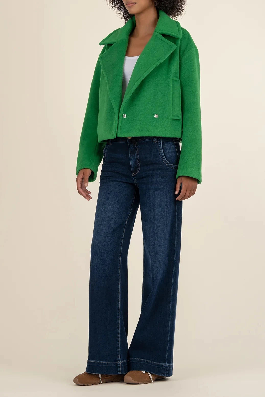 Person wearing a green jacket and blue jeans on a beige background