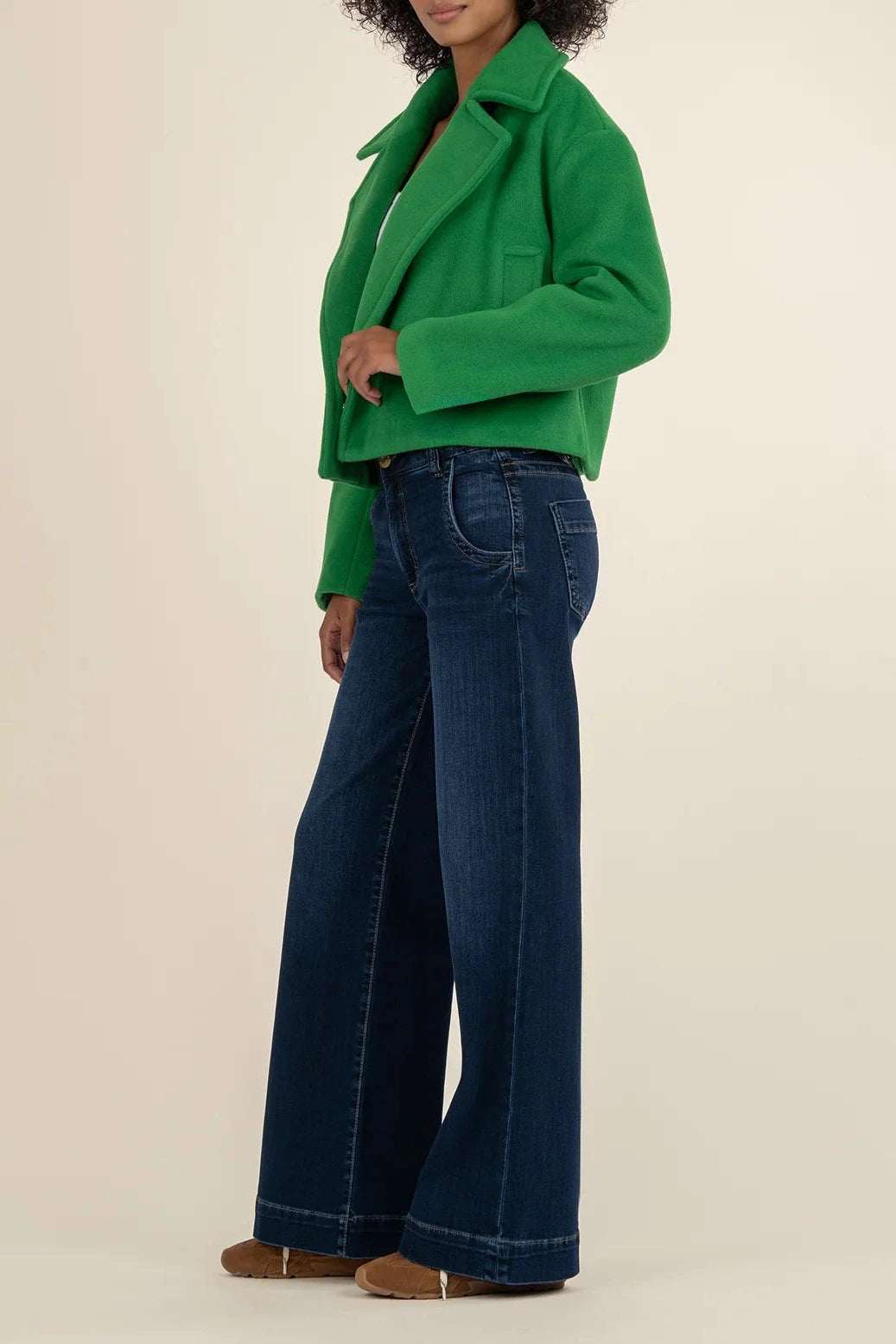 Person wearing a green jacket and blue jeans on a beige background