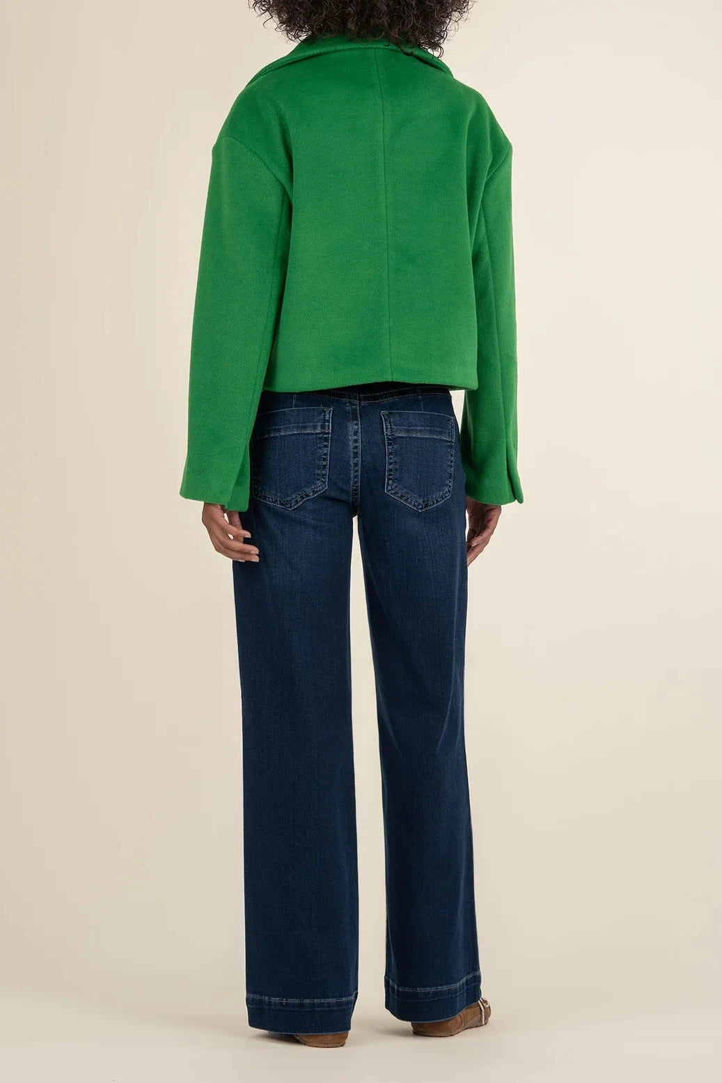 Person wearing a green jacket and blue jeans on a beige background