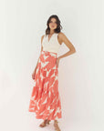 Woman wearing a white top and coral patterned skirt on a white background