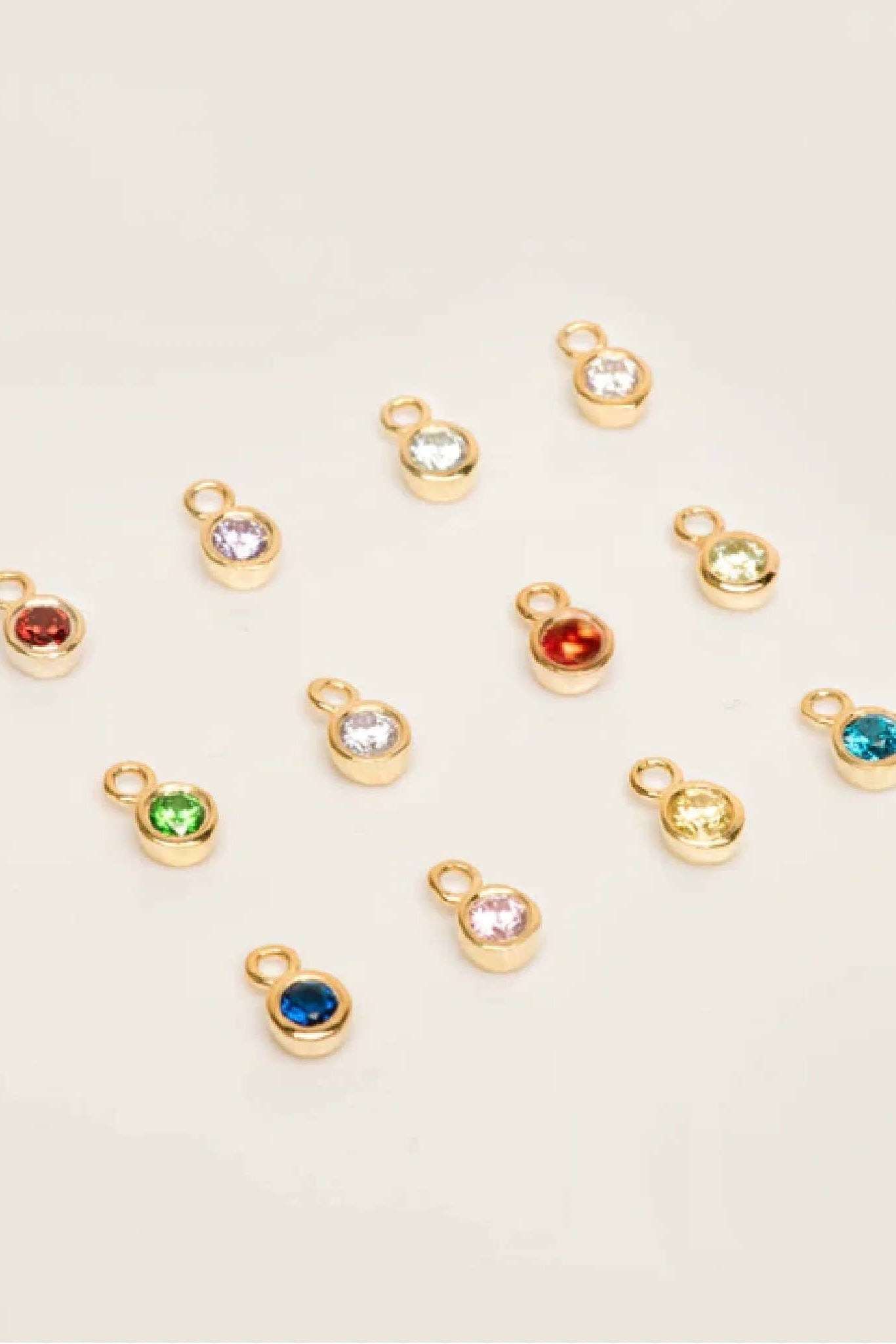 Gold charm pendants with colored gemstones on a beige background