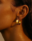 Close-up of a person wearing a gold hoop earring with a warm brown background