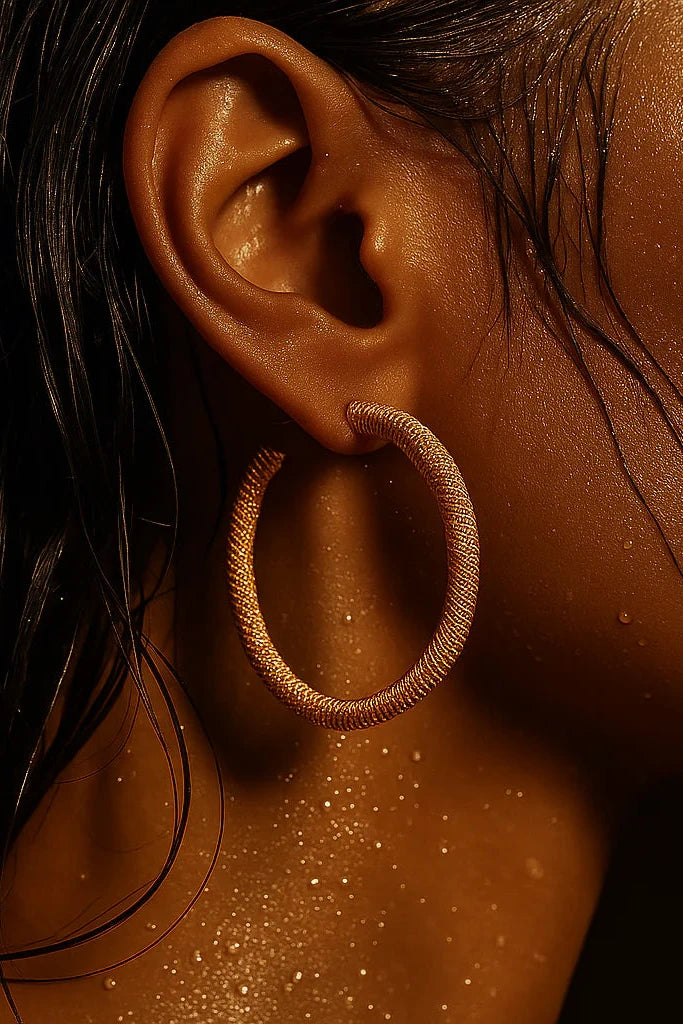 Close-up of an ear wearing a gold hoop earring with a dark background