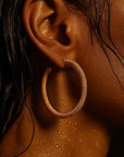Close-up of an ear wearing a gold hoop earring with a dark background