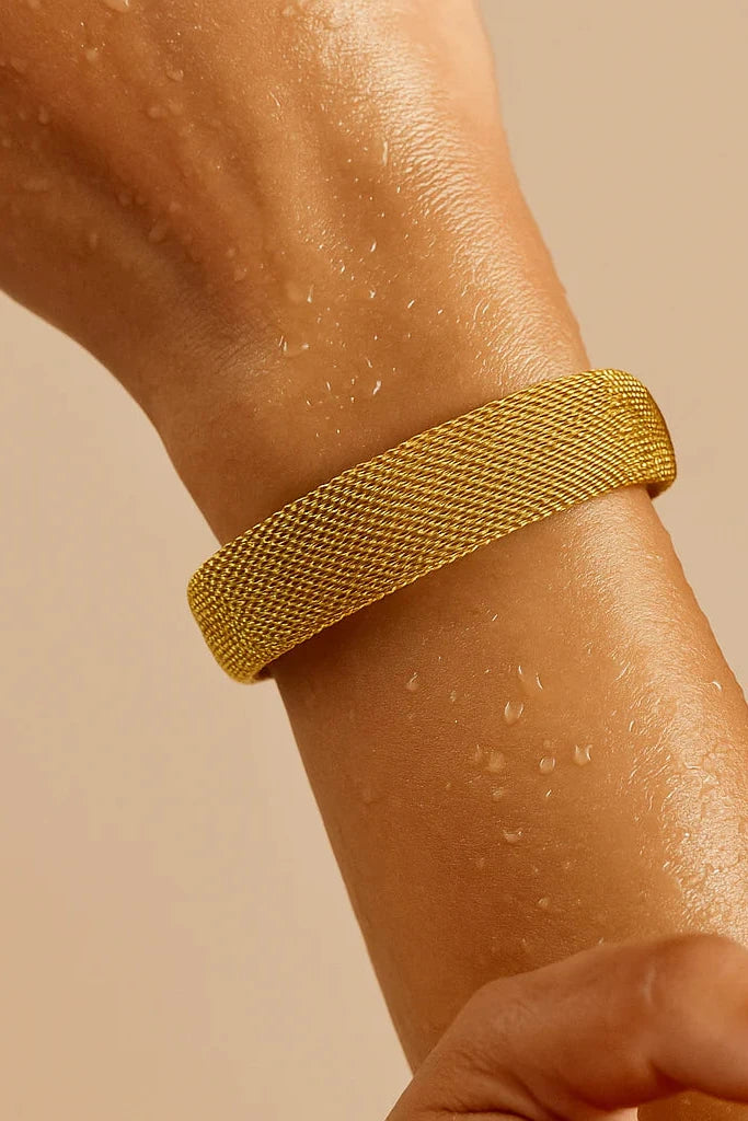 Gold mesh bracelet on a wrist against a beige background