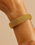 Gold mesh bracelet on a wrist against a beige background