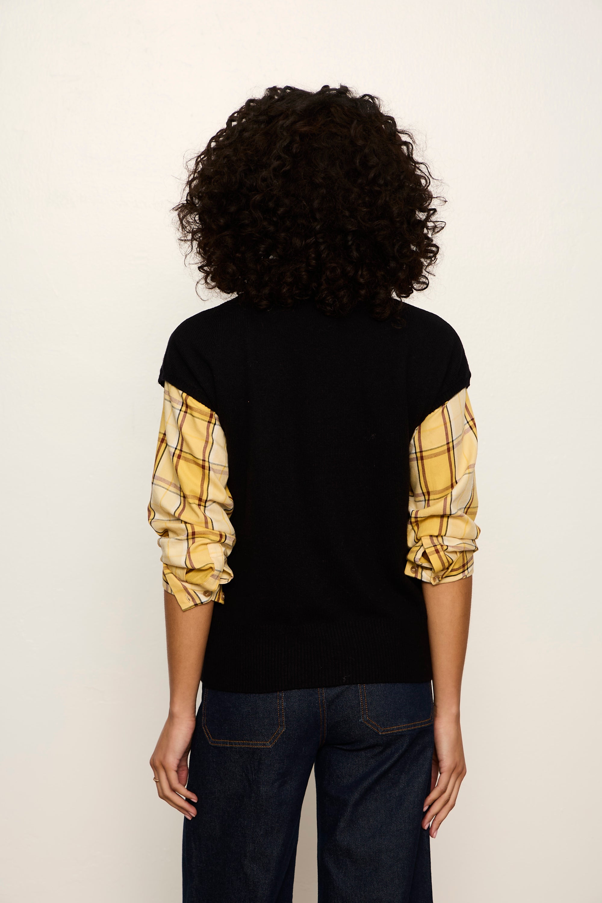 Person wearing a black sweater with yellow plaid sleeves on a white background