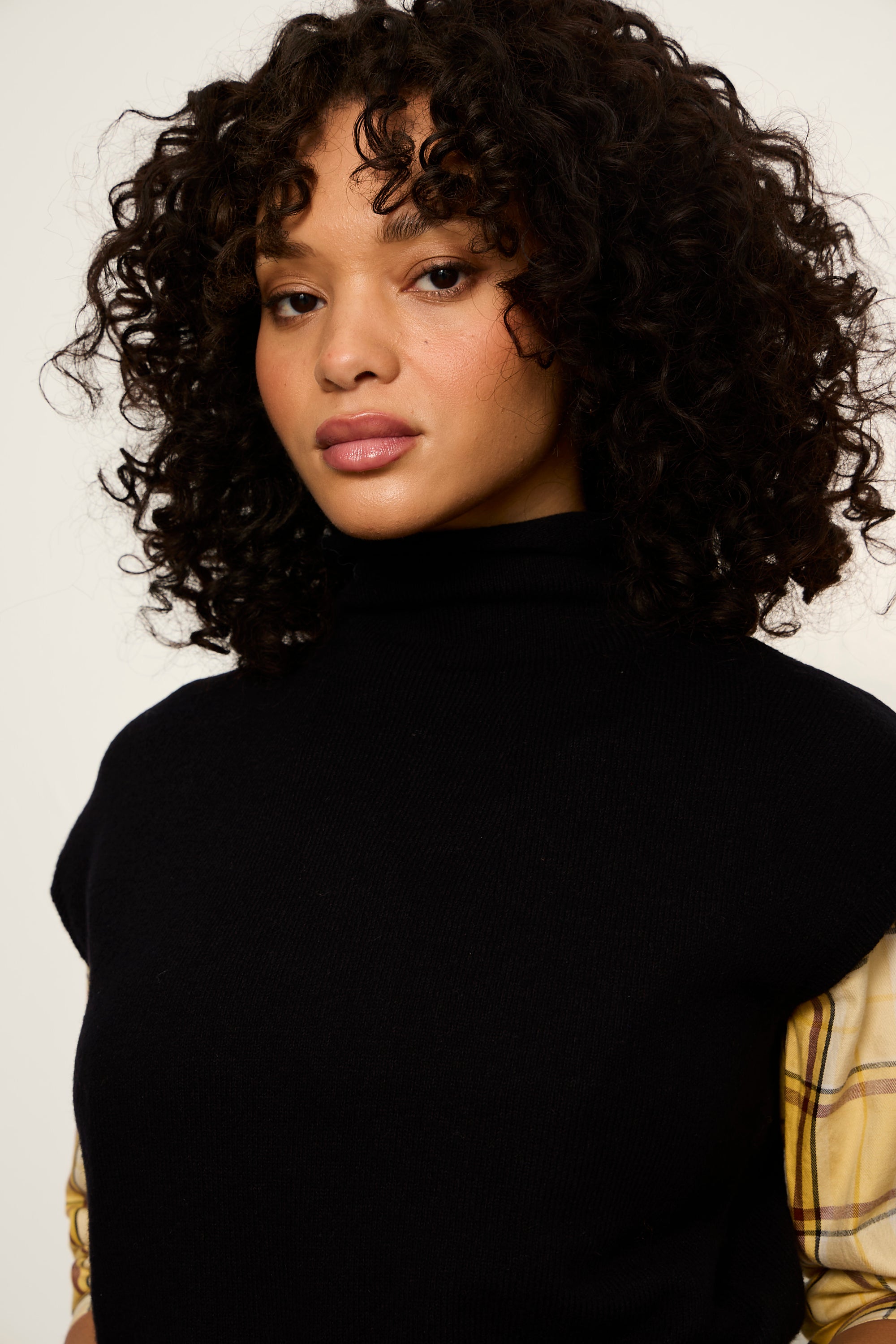 Woman with curly hair wearing a black turtleneck against a white background
