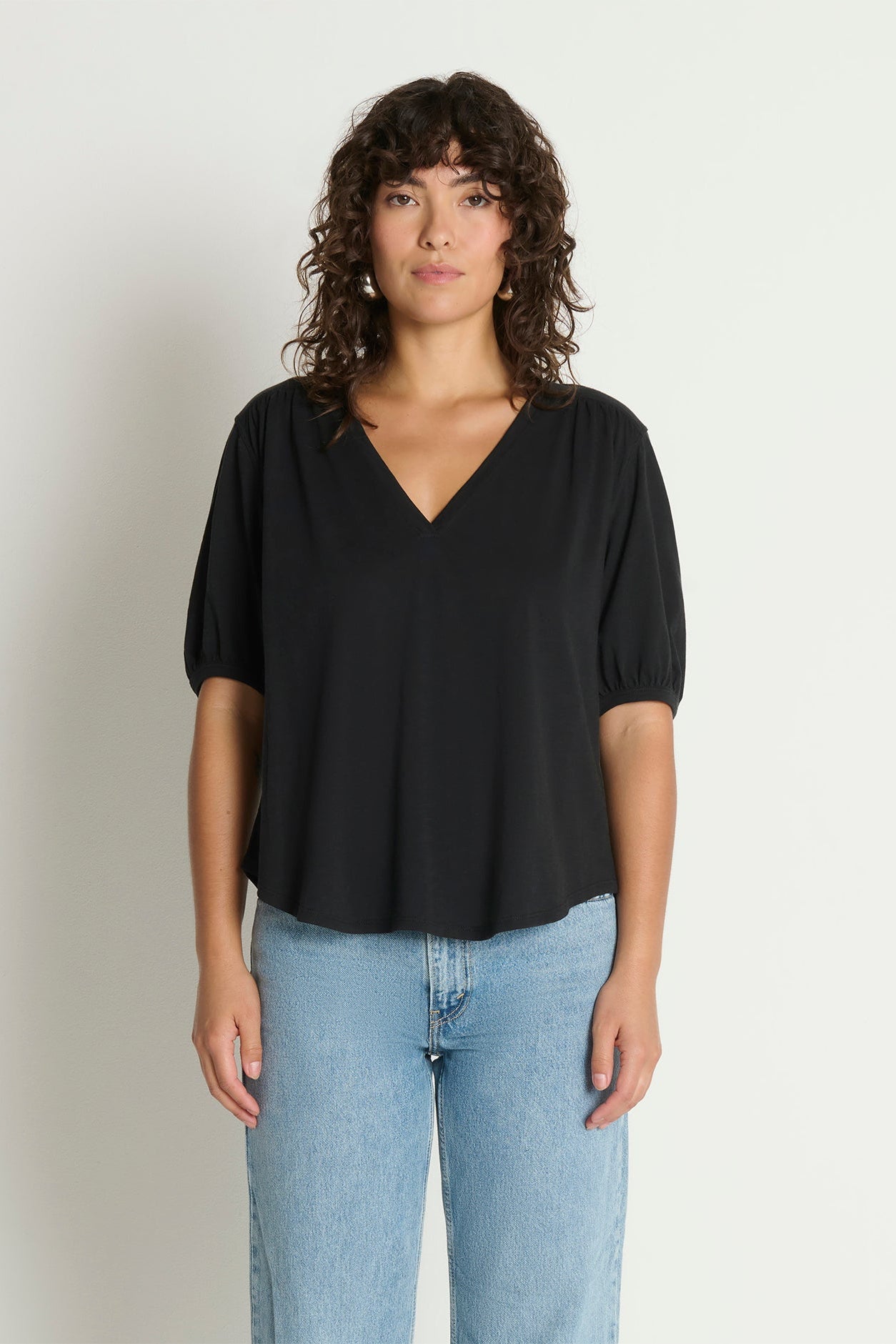 Woman wearing a black top and blue jeans against a plain background