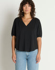 Woman wearing a black top and blue jeans against a plain background