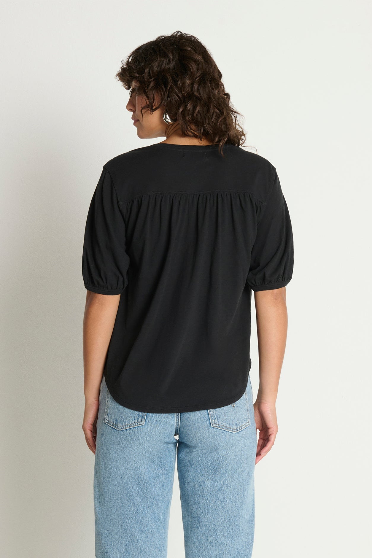 Person wearing a black top and light blue jeans on a plain background