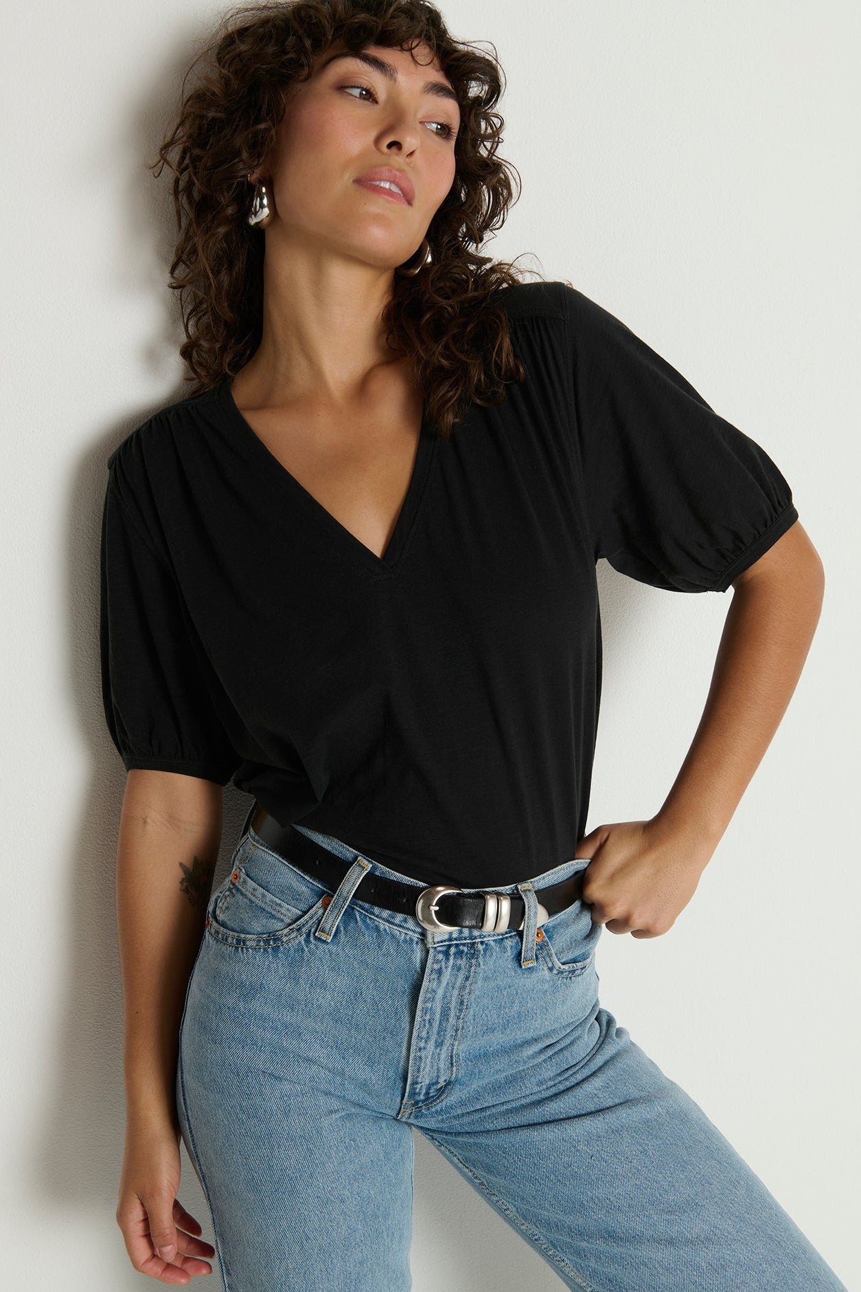 Woman wearing a black top and blue jeans against a plain background