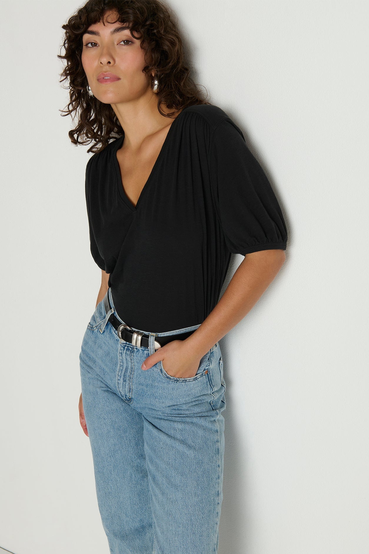 Woman wearing a black top and blue jeans against a plain background