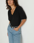 Woman wearing a black top and blue jeans against a plain background
