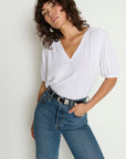Woman wearing a white top and blue jeans against a plain background