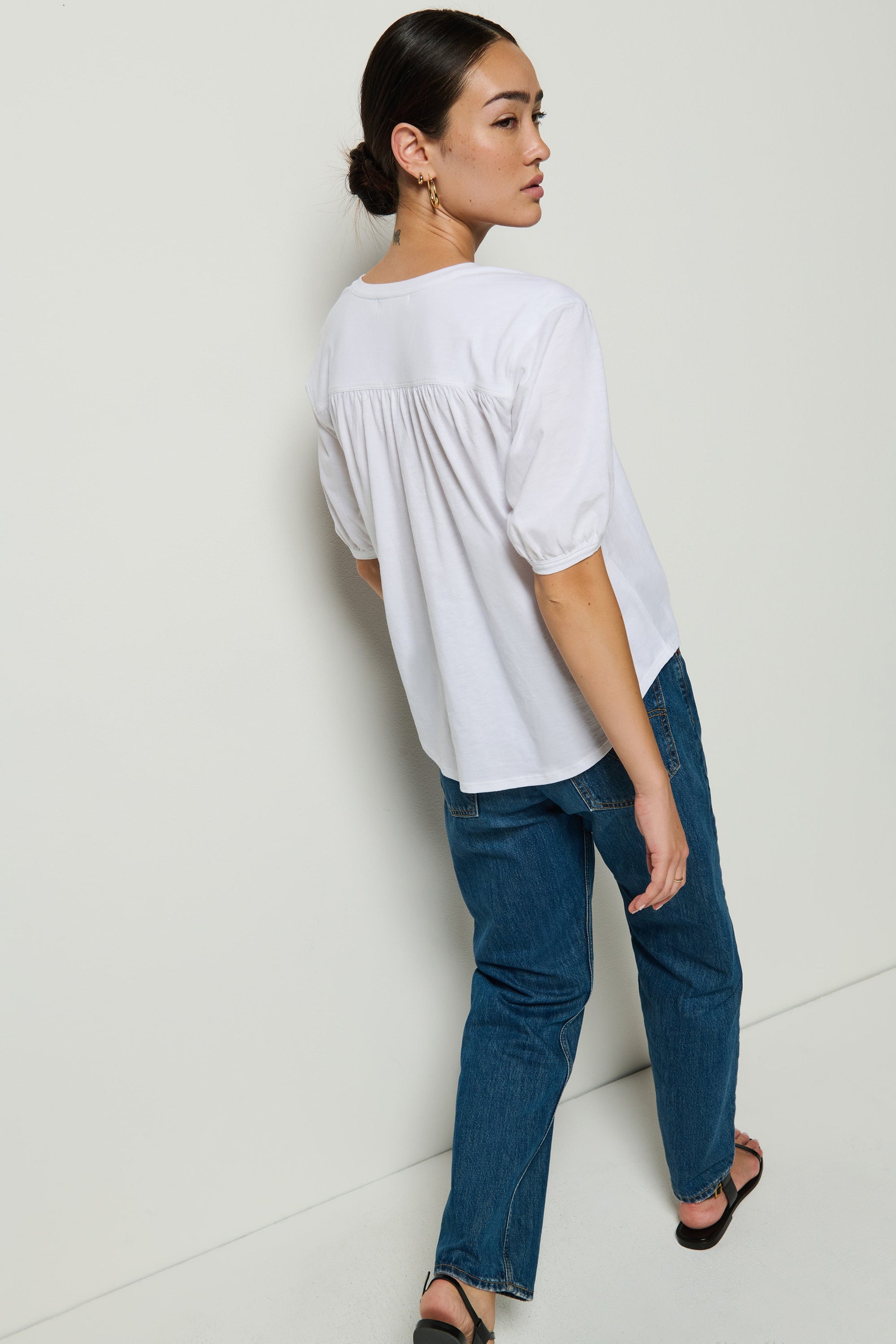 Woman wearing a white blouse and blue jeans against a white wall.