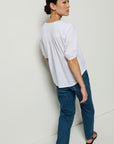Woman wearing a white blouse and blue jeans against a white wall.