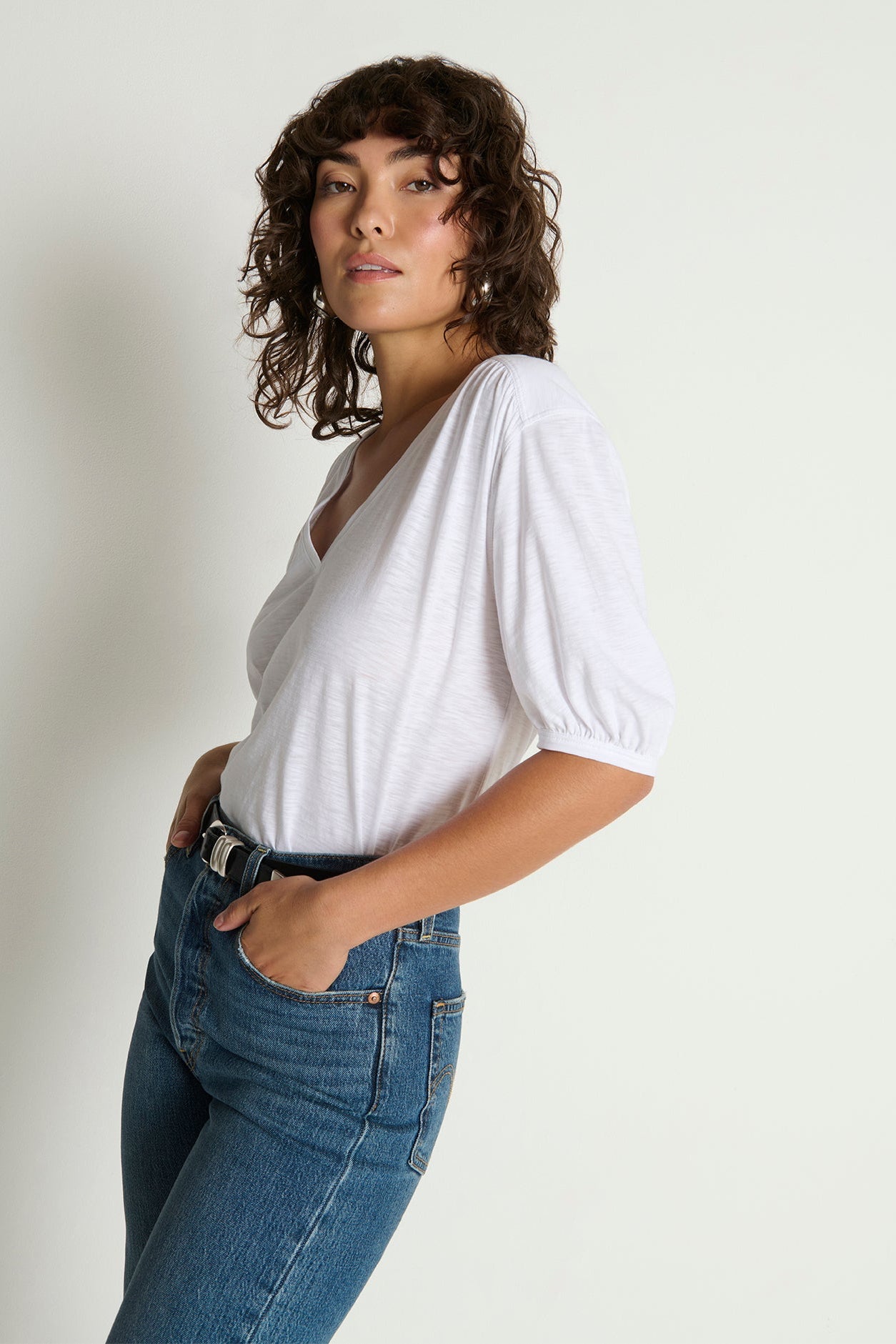 Woman wearing a white t-shirt and blue jeans against a plain background