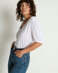 Woman wearing a white t-shirt and blue jeans against a plain background