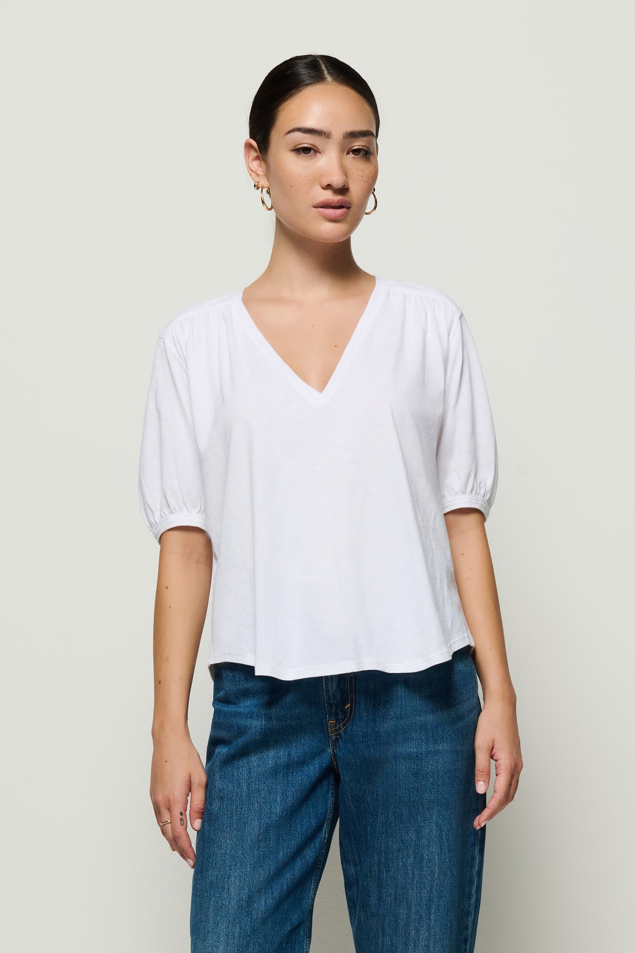 Woman wearing a white blouse and blue jeans against a plain background