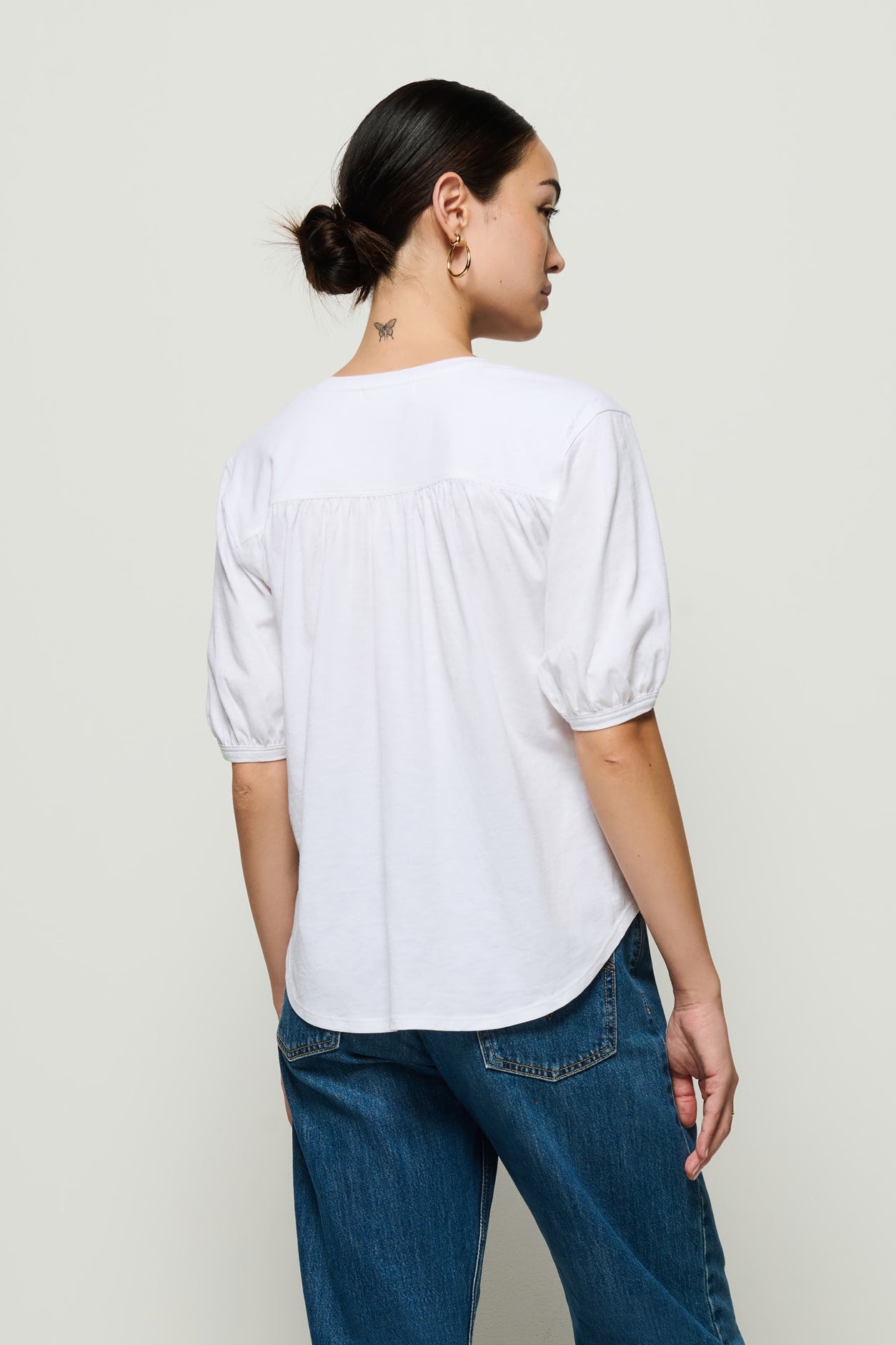 Person wearing a white blouse and blue jeans against a plain background