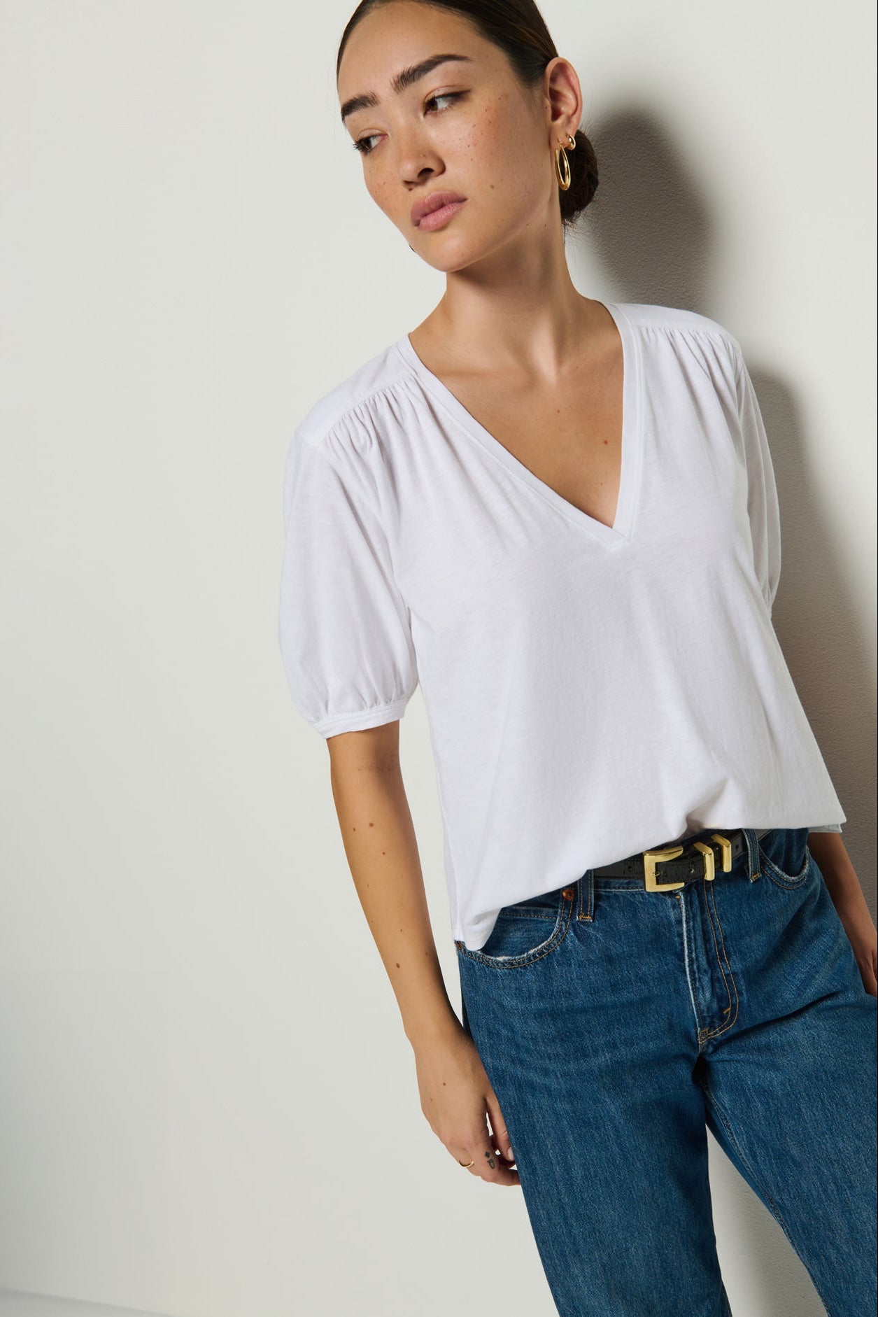 Woman wearing a white blouse and blue jeans against a plain background