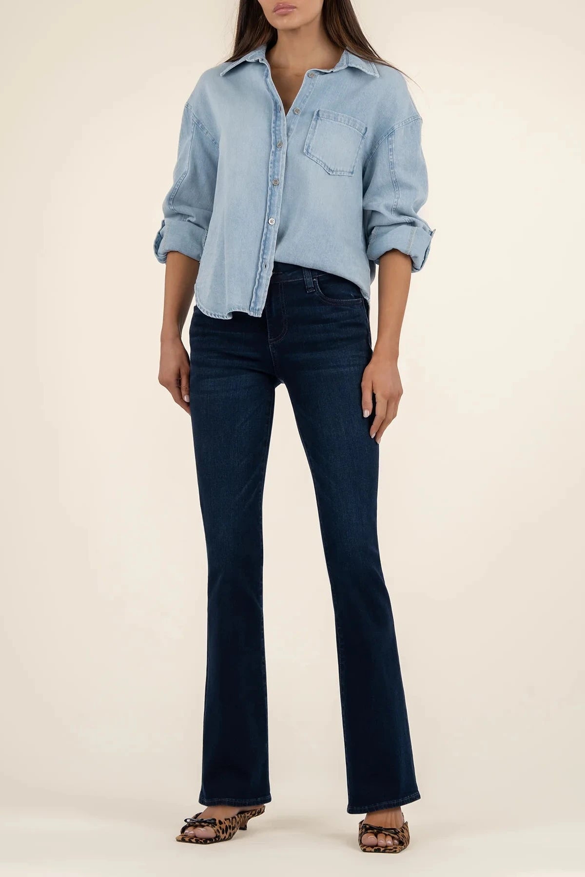 Person wearing a light blue denim shirt and dark blue jeans on a beige background