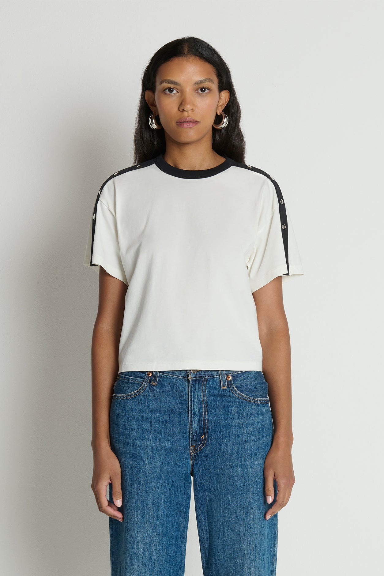 Woman wearing a white t-shirt with black accents and blue jeans on a plain background