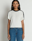 Woman wearing a white t-shirt with black accents and blue jeans on a plain background