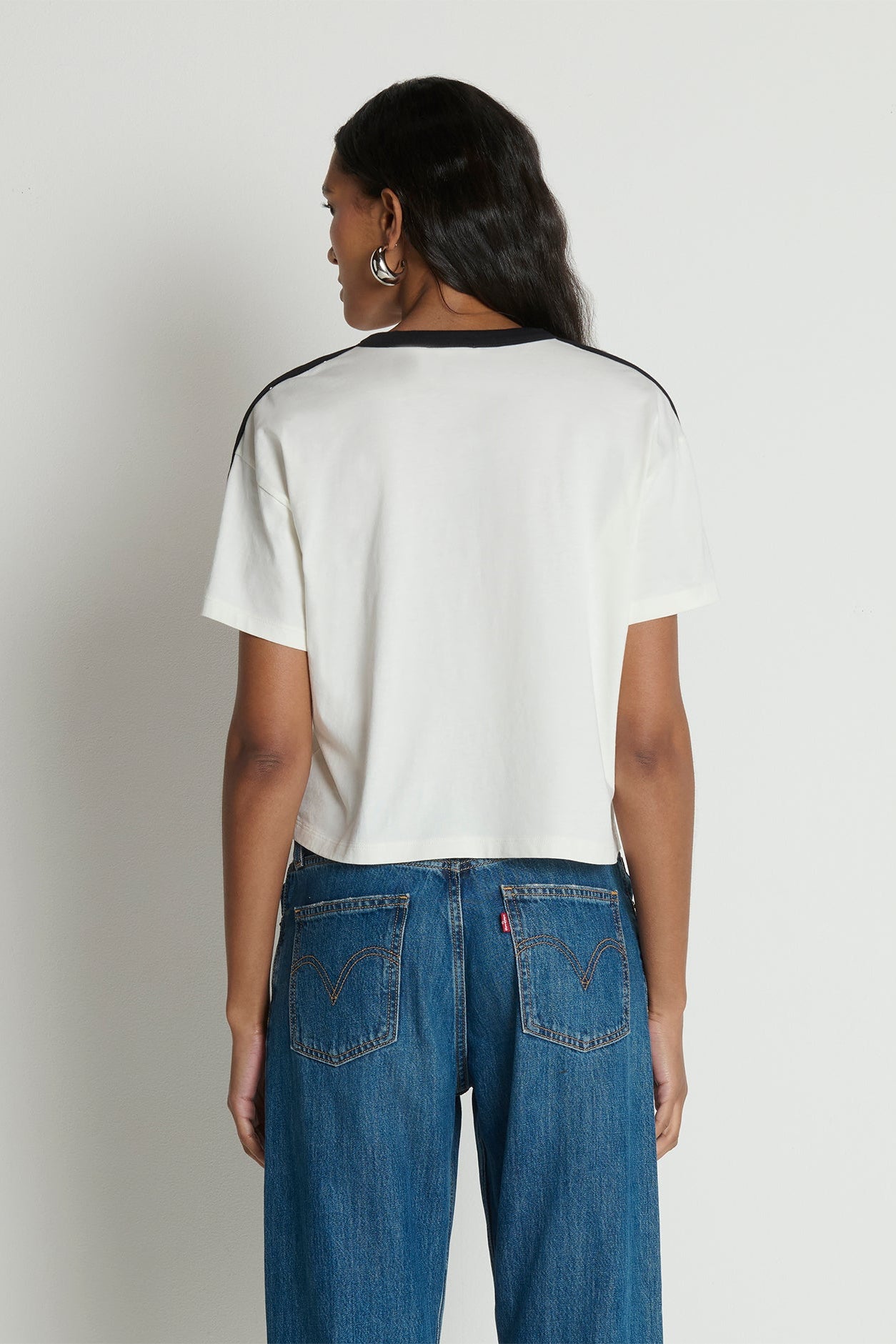 Person wearing a white t-shirt with black trim and blue jeans on a plain background