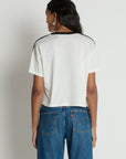 Person wearing a white t-shirt with black trim and blue jeans on a plain background