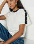 Woman wearing a white t-shirt with black trim and buttons, sitting against a white background