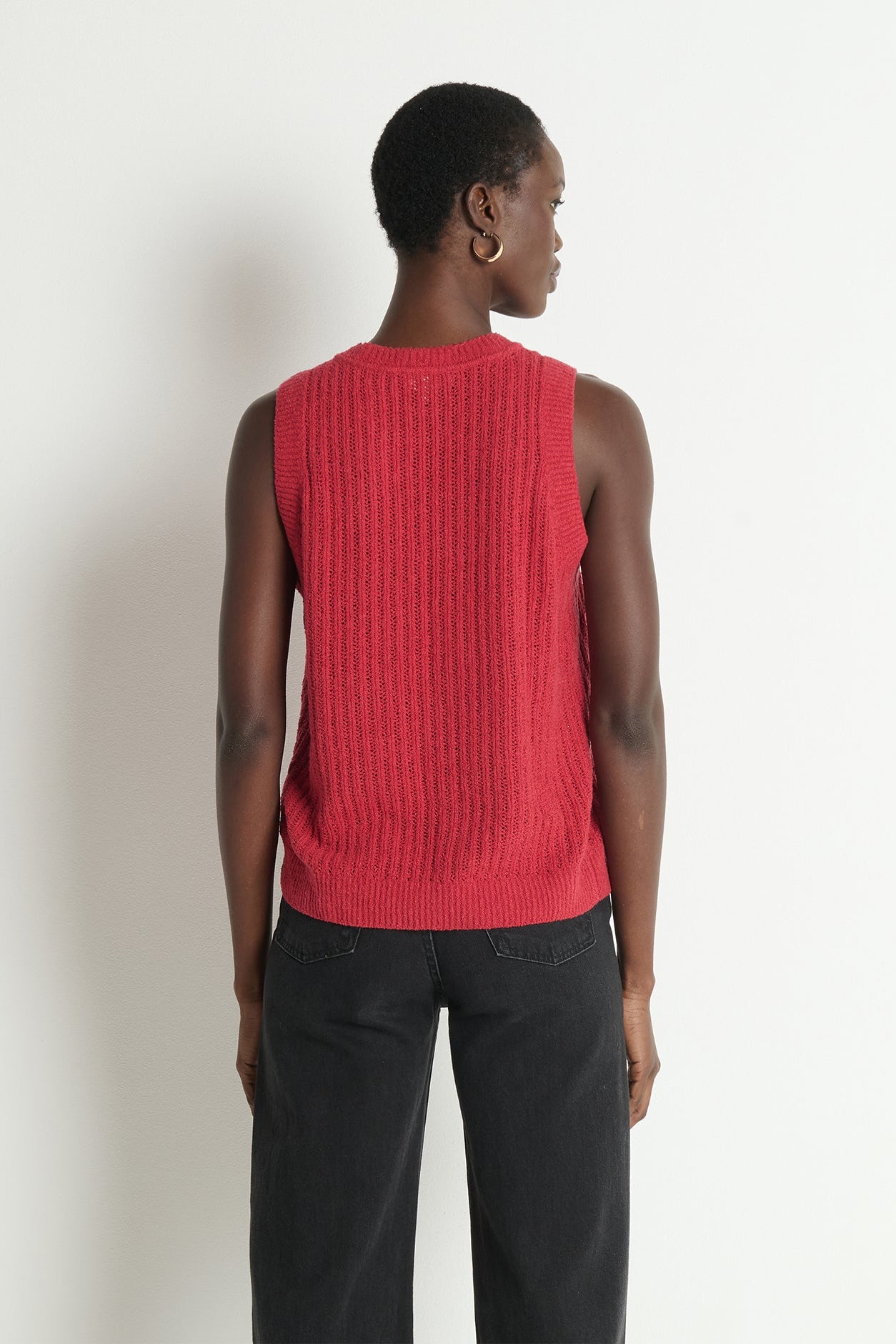 Person wearing a red sleeveless knitted top against a white background