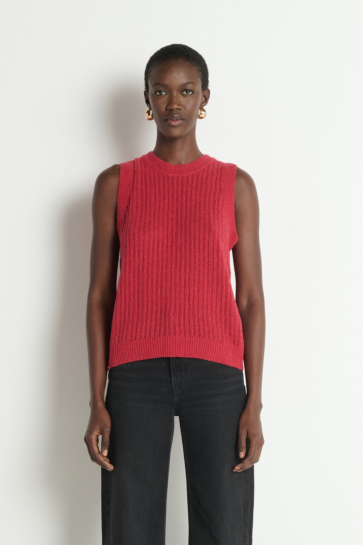 Woman wearing a red sleeveless knitted top against a white background