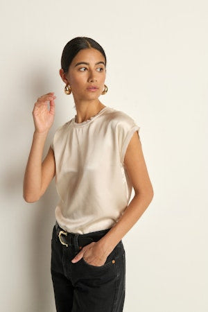 Woman wearing a beige sleeveless top and black pants against a plain background