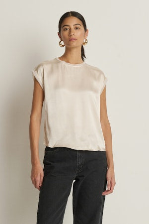 Woman wearing a beige sleeveless top and black pants against a plain background