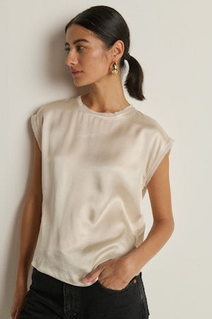 Woman wearing a beige sleeveless top against a plain background