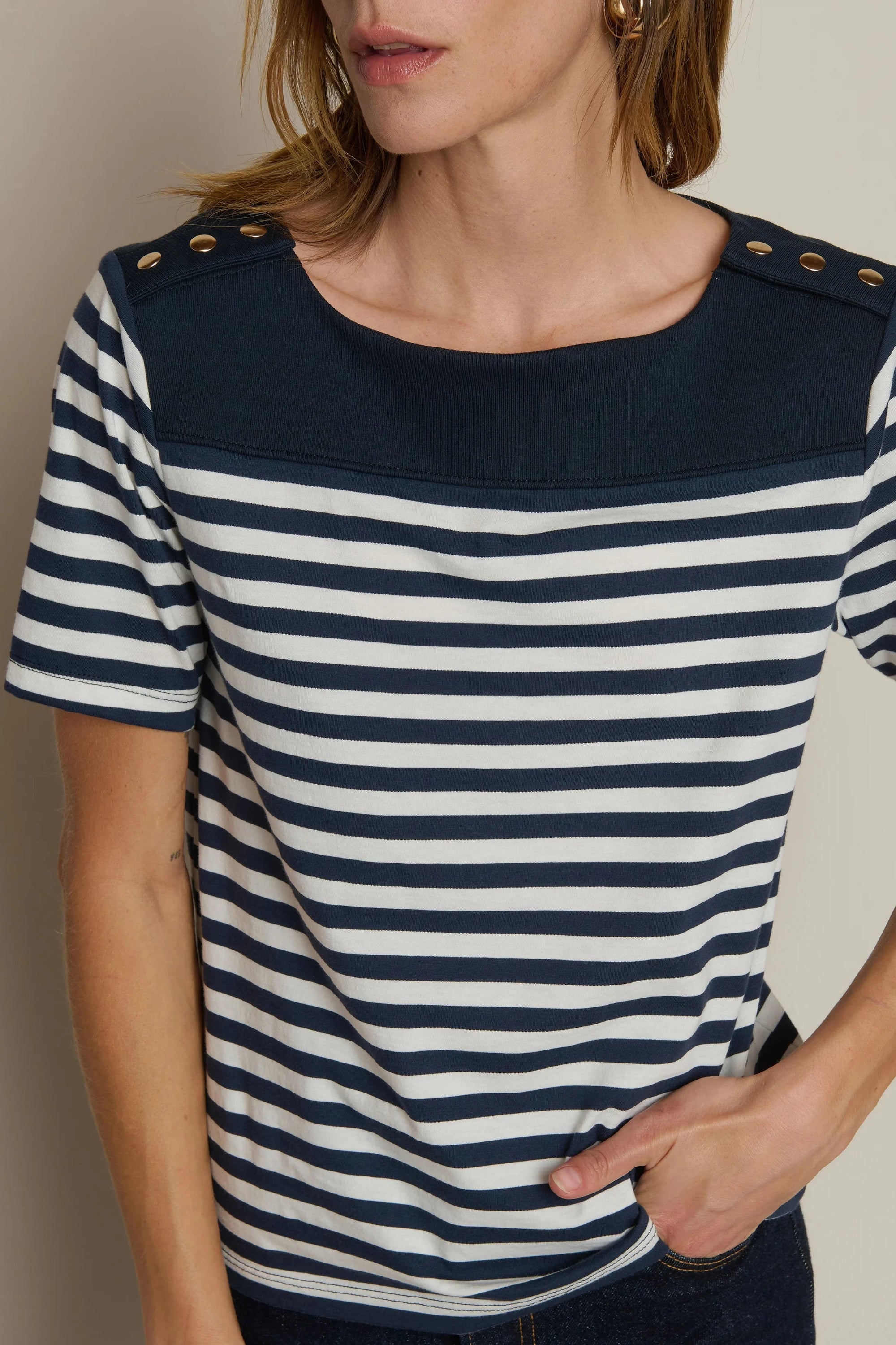 Woman wearing a navy and white striped shirt with button details on a plain background