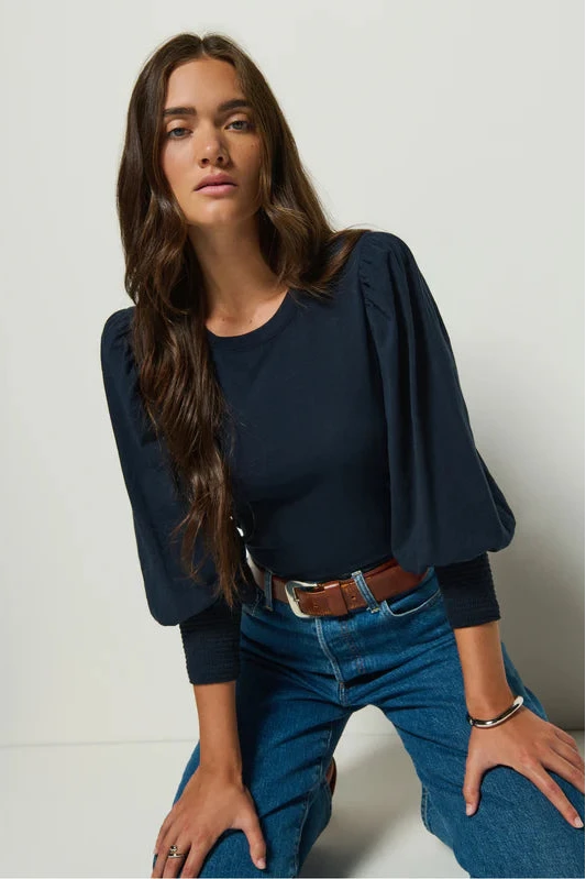 Woman wearing a navy blazer and blue jeans against a plain background