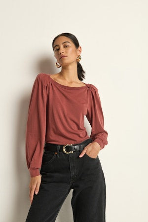 Woman wearing a rust-colored blouse and black pants against a beige wall