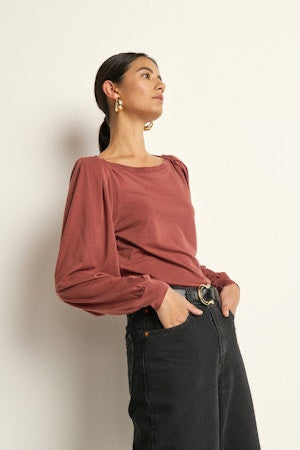 Woman wearing a rust-colored top and black pants against a beige background