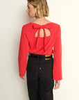 Woman wearing a red blouse with a bow detail on the back against a white wall