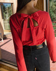 Person wearing a red blouse with a bow detail and black pants outdoors.