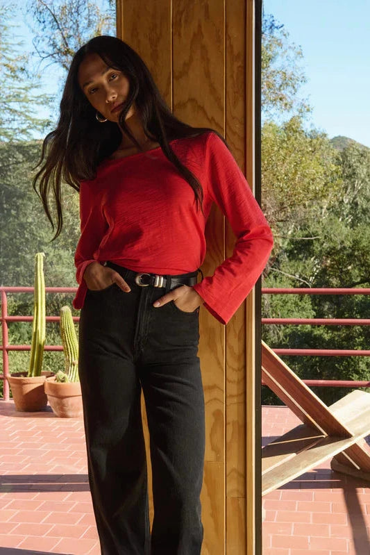 Woman in a red sweater and black pants standing on a deck with greenery in the background