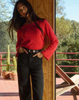 Woman in a red sweater and black pants standing on a deck with greenery in the background