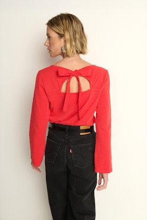 Person wearing a red blouse with a bow detail on the back against a plain background