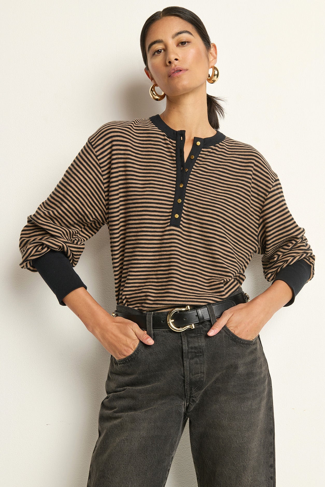 Woman wearing a striped shirt and dark jeans against a plain background